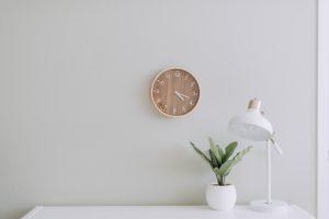 White wall with a clock on the wall and a lamp on a white desk.